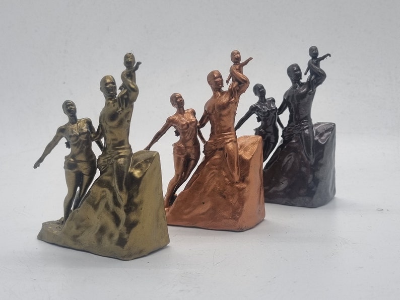 May include: Three bronze-colored sculptures of families, each with a parent holding a child. The sculptures are on a textured base and are arranged in a row from left to right.