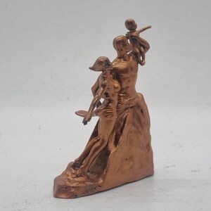 May include: A bronze-colored sculpture of a family. The father is holding a child on his shoulders, while the mother stands beside him. The sculpture is on a base that resembles a rock.