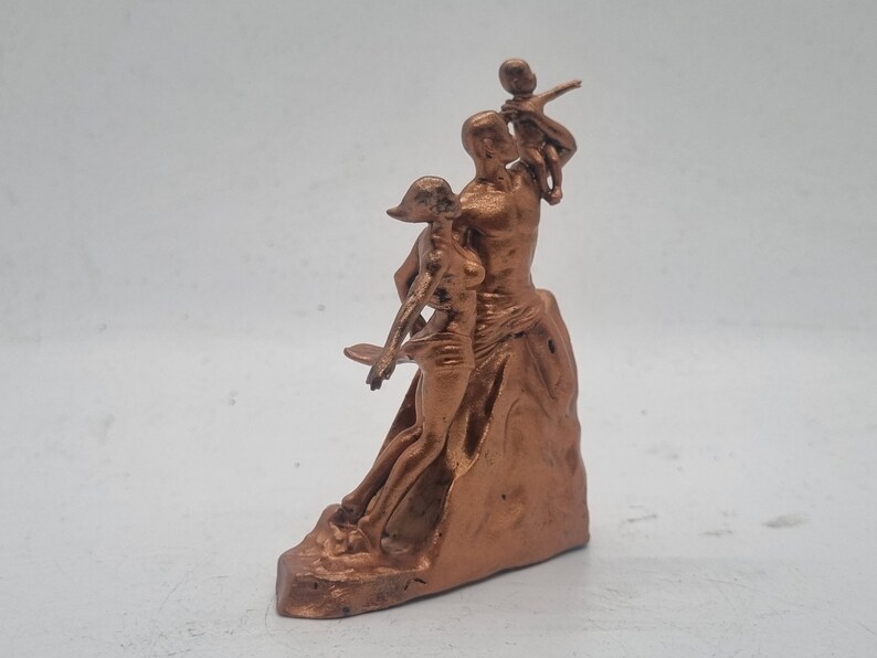 May include: A bronze-colored sculpture of a family. The father is holding a child on his shoulders, while the mother stands beside him. The sculpture is on a base that resembles a rock.