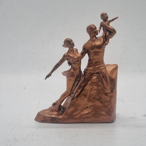 May include: A bronze-colored sculpture of a family. The sculpture depicts a man holding a child up in the air, while a woman stands next to him. The sculpture is on a base that resembles a rock.