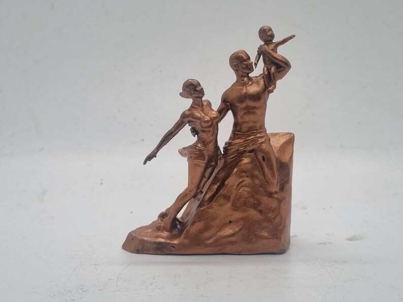 May include: A bronze-colored sculpture of a family. The sculpture depicts a man holding a child up in the air, while a woman stands next to him. The sculpture is on a base that resembles a rock.