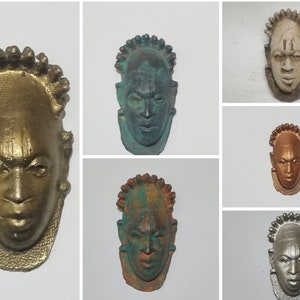 Op de afbeelding: Zes kleine, decoratieve maskers met verschillende verf afwerkingen. De maskers zijn gemaakt van een getextureerd materiaal en hebben een menselijk gezicht met een kroon van kralen bovenop het hoofd.