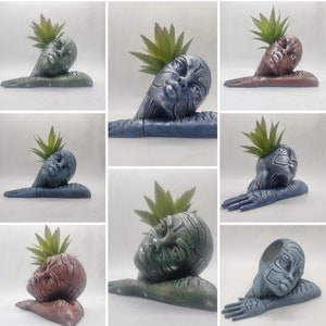 Puede incluir: Un conjunto de diez macetas únicas, cada una con un rostro humano estilizado con una planta que crece de la cabeza. Las macetas están hechas de un material liso y gris y están disponibles en una variedad de colores.