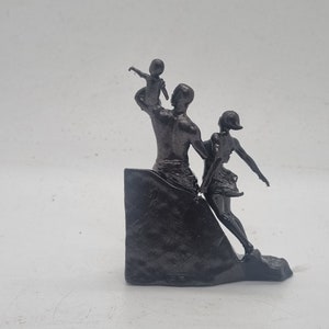 May include: A black metal sculpture of a family. The father is holding a child up in the air, while the mother is walking beside him. The sculpture is on a black base.