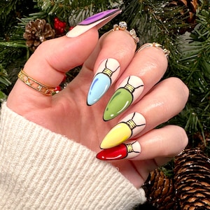 Peut inclure: Gros plan sur une main avec de longs ongles en amande peints d'une base blanche et des motifs d'ampoules. Les ampoules sont peintes dans différentes couleurs, notamment le bleu, le vert, le jaune et le rouge.
