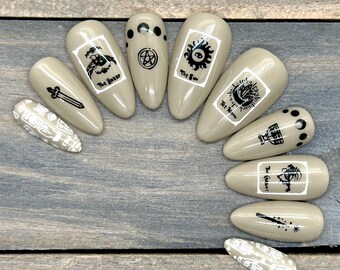 May include: Ten nude-colored artificial fingernails with black and white tarot card designs. The designs include The Tower, The Sun, The Lovers, The Chariot, The Emperor, The Hanged Man, The World, The Star, The Moon, and The Devil.