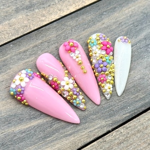 Puede incluir: Cinco u&ntilde;as postizas de color rosa en forma de stiletto con intrincados dise&ntilde;os florales. Cada u&ntilde;a est&aacute; adornada con peque&ntilde;as flores de colores y cuentas doradas.