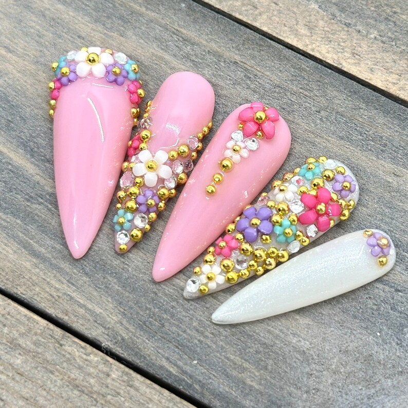 Puede incluir: Cinco u&ntilde;as de stiletto rosas y blancas con adornos de flores doradas y coloridas.