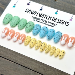 May include: Set of 10 press-on nails with an Easter theme. The nails are decorated with pastel blue, green, and yellow speckled egg designs. Some nails feature white bunny ears.
