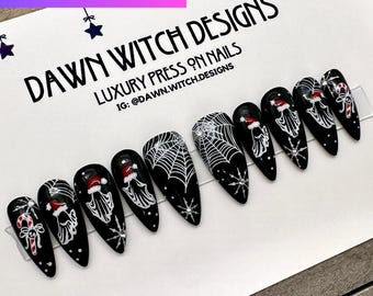 May include: Black press-on nails with white spiderwebs and ghosts wearing Santa hats. The nails are decorated with rhinestones.  IG: @DAWN.WITCH.DESIGNS