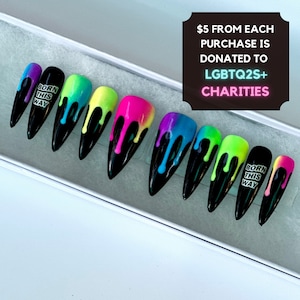 Op de afbeelding: Set van tien zwarte stiletto kunstnagels met een druppelend regenboogontwerp. Elke nagel heeft een andere kleurencombinatie van roze, geel, groen, blauw en paars. Eén nagel heeft de tekst "Born This Way".