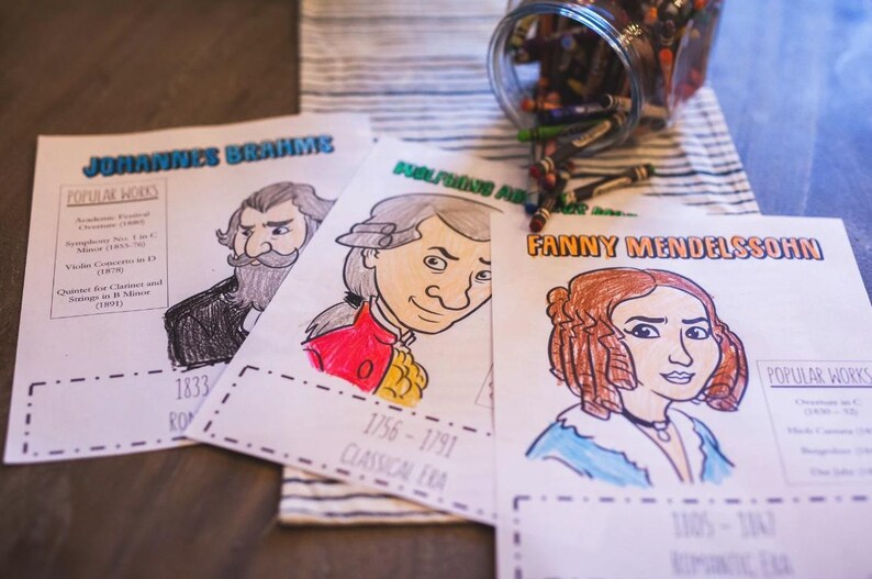 Puede incluir: P&aacute;ginas para colorear con retratos de Johannes Brahms, Wolfgang Amadeus y Fanny Mendelssohn, con texto que indica sus nombres y &eacute;pocas. Un tarro de crayones es visible en el fondo. Las p&aacute;ginas est&aacute;n parcialmente coloreadas.