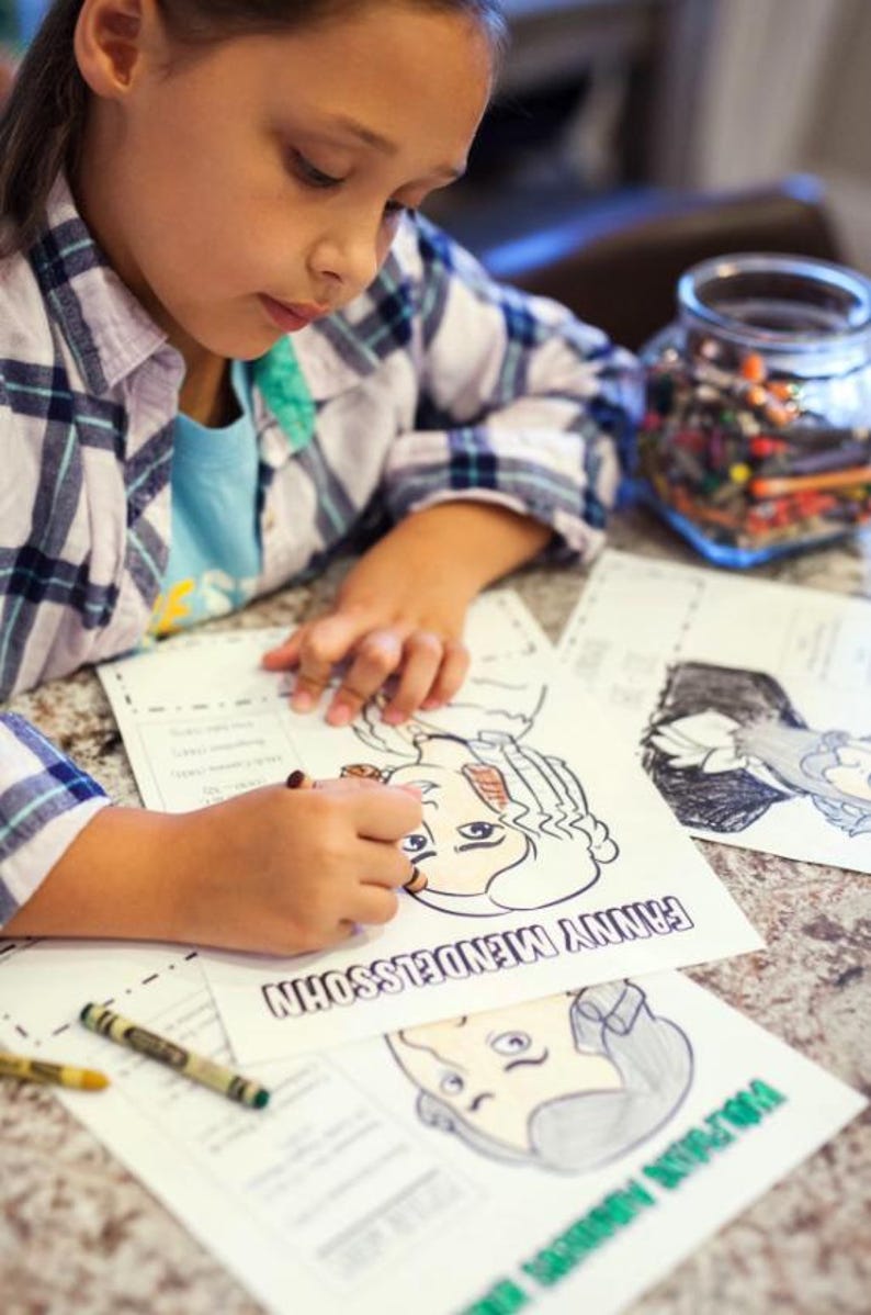 Puede incluir: Un ni&ntilde;o colorea un dibujo en blanco y negro de una persona con el texto "FANNY MENDELSSOHN" en la p&aacute;gina. Creyones y un tarro de l&aacute;pices de colores est&aacute;n cerca. El ni&ntilde;o lleva una camisa a cuadros.