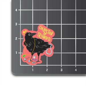 May include: A pink sticker with a black crow wearing a necklace of trinkets. The crow is looking to the left. The sticker says "Collector of Trinkets" in yellow text.