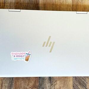 May include: A silver laptop with a sticker that says "Overstimulated & Highly Caffeinated" with a cartoon image of a boba tea drink.
