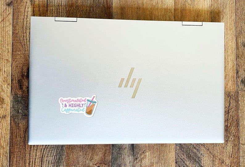 May include: A silver laptop with a sticker that says "Overstimulated & Highly Caffeinated" with a cartoon image of a boba tea drink.