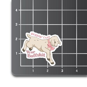 May include: A white lamb with a pink bow, jumping over the text "Hoppin' Over Your Bullshit".