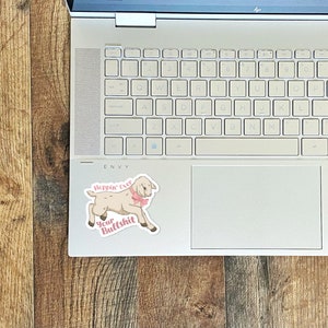 May include: A white goat with a pink bow sticker on a laptop. The sticker says "Hoppin' Over Your Bullshit".