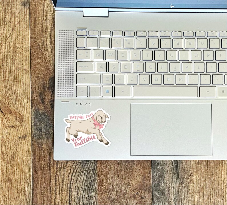 May include: A white goat with a pink bow sticker on a laptop. The sticker says "Hoppin' Over Your Bullshit".