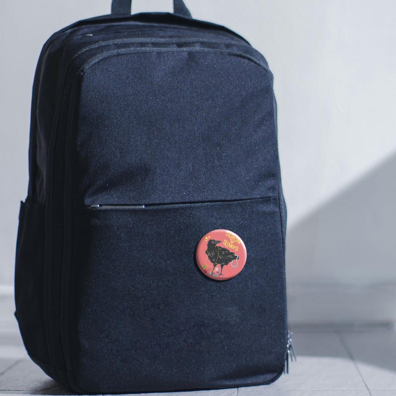 May include: A navy blue backpack with a small, round button pinned to the front. The button is red with a black crow illustration and the text "Crow Rukes" in yellow.