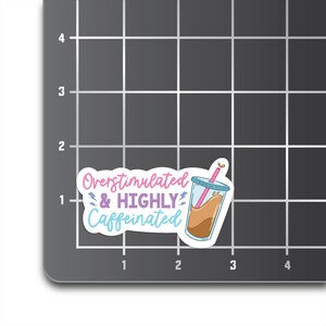 May include: A white sticker with a pink, blue, and purple graphic of a coffee cup with a straw and the text "Overstimulated & HIGHLY Caffeinated".