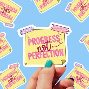 May include: A yellow sticky note with pink and purple tape and stars. The note says "Progress not Perfection" in pink lettering with a pink arrow.
