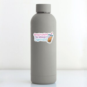 May include: A gray water bottle with a sticker that says "Overstimulated & Highly Caffeinated" with a cartoon image of a glass of iced coffee with a pink straw.