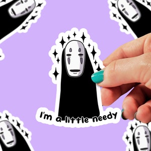 May include: A sticker featuring a black and white illustration of No Face from the movie Spirited Away. The character is surrounded by sparkling stars and the text "I'm a little needy" is below the character.