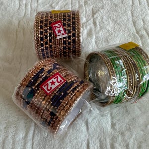 May include: Three sets of bangles, one set is green, one set is blue and gold, and the other set is blue and gold with a red star sticker that says "2+".