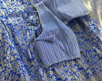 May include: A blue and silver brocade fabric with a floral and bird pattern. A matching blue and silver brocade blouse is draped over the fabric.