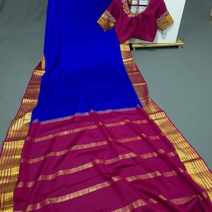 May include: A blue and magenta silk saree with a gold border. The saree has a contrasting magenta pallu with gold stripes. The saree is paired with a magenta blouse with gold embroidery.