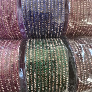 May include: A set of colorful bangles with rhinestones. The bangles are in shades of pink, purple, green, and black. The bangles are packaged in clear plastic.