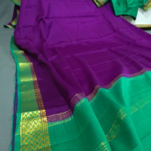 May include: A vibrant purple saree with a green border and gold accents. The saree is paired with a green blouse with gold embroidery. The fabric appears to be smooth and flowing, with a rich color palette.