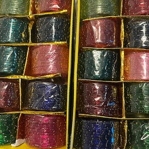 May include: Two rectangular boxes containing multiple stacks of thin, circular bangles in various translucent colors including red, green, blue, and pink. Each bangle features small, evenly spaced gold-colored glitter accents throughout.