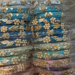 May include: A stack of blue and pink bangle bracelets with gold and pearl embellishments. The bracelets are wrapped in clear plastic.