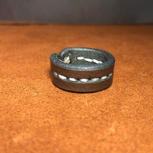May include: A grey leather ring with white stitching.