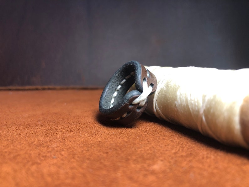 May include: A brown leather ring with white stitching. The ring is lying on a brown surface.