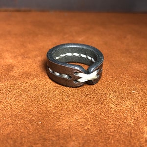 May include: A black leather ring with white stitching. The stitching is in a criss-cross pattern.
