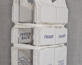 May include: A white canvas life vest in a clear acrylic display case. The vest is labeled "Inside Back" and "Front" on the different sections. The vest is also labeled "Warranted to Pass Board of Trade" and "Fosbery & Co. Life Buoys Rich St. Limehouse, London".