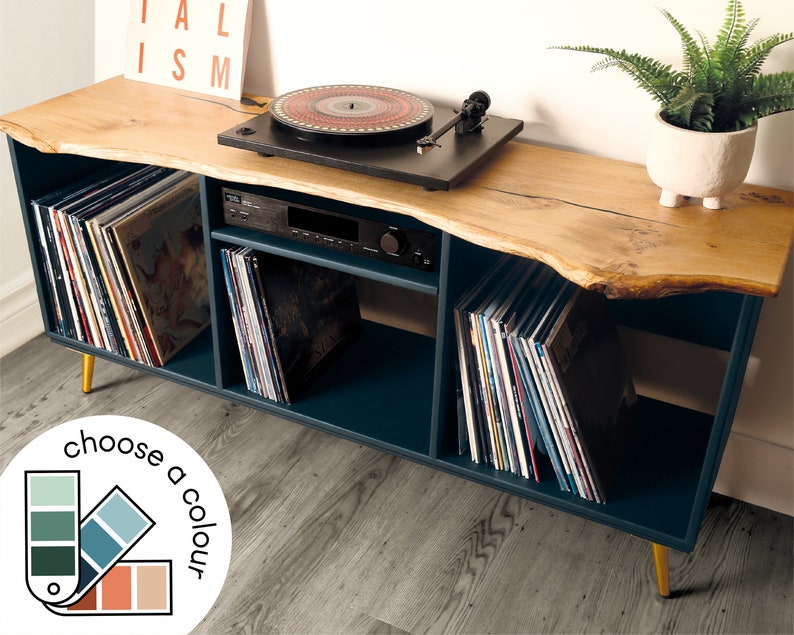 Może przedstawiać: Stojak na gramofon w kolorze turkusowym z blatem z drewna o żywym brzegu. Stojak ma cztery p&oacute;łki do przechowywania płyt winylowych i złote n&oacute;żki. Stojak stoi na drewnianej podłodze.
