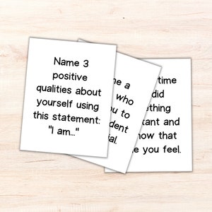 May include: Three white cards with black text. The first card says "Name 3 positive qualities about yourself using this statement: "I am..."