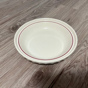May include: A white ceramic pie plate with a red rim. The plate has a fluted edge.