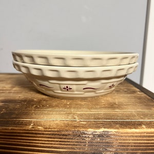 May include: Two white ceramic bowls with a red and white floral design. The bowls are stacked on top of each other.