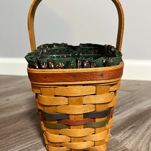 May include: A woven basket with a green floral fabric lining and a wooden handle. The basket has a brown, red, green, and blue trim.