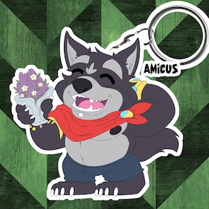 Puede incluir: Un llavero con un personaje de lobo de dibujos animados con una bufanda roja, pantalones cortos azules y un ramo de flores moradas. La palabra "Amicus" está impresa en el llavero.