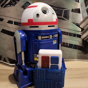 May include: A white ceramic mug with a black handle and the text "But First, Coffee" in a black, handwritten-style font. The mug is on a white surface.