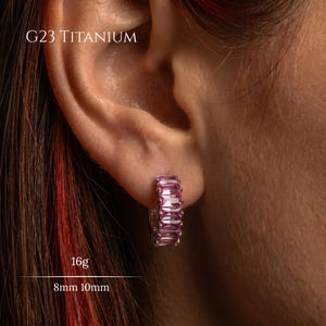 Könnte beinhalten: Nahaufnahme eines Ohrs mit einem G23 Titan-Creolen-Ohrring. Der silberne Ohrring ist mit rechteckigen rosa Edelsteinen besetzt. Der Text "G23 Titanium", "16g" und "8mm 10mm" ist im Bild enthalten.