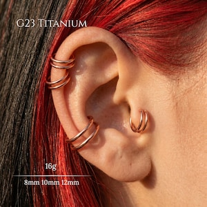 May include: An ear featuring multiple rose gold hoop earrings. The image includes text that reads "G23 Titanium", "16g", and measurements of 8mm, 10mm, and 12mm. The hair in the background is black and red.