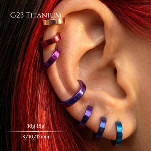May include: A series of six G23 titanium hoop earrings in a gradient of colors including rose gold, red, purple, and blue, worn along the outer edge of an ear. The text G23 TITANIUM, 16g 18g, and 8/10/12mm is visible on the image.