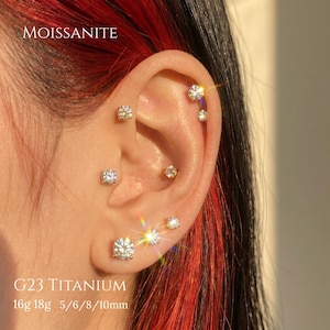 Op de afbeelding: Een set ronde, briljant geslepen moissaniet oorknopjes gezet in G23 titanium. De sieraden bestaan uit meerdere heldere, sprankelende stenen gedragen in diverse oorpiercings, met de tekst MOISSANITE, G23 TITANIUM, 16g 18g 5/6/8/10mm.